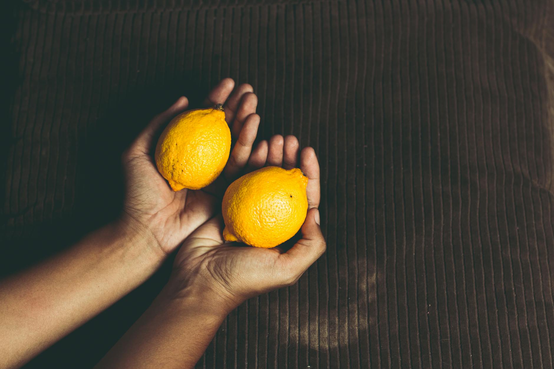Mains tenant des citrons frais sur un fond marron, symbolisant la santé et le renouvellement