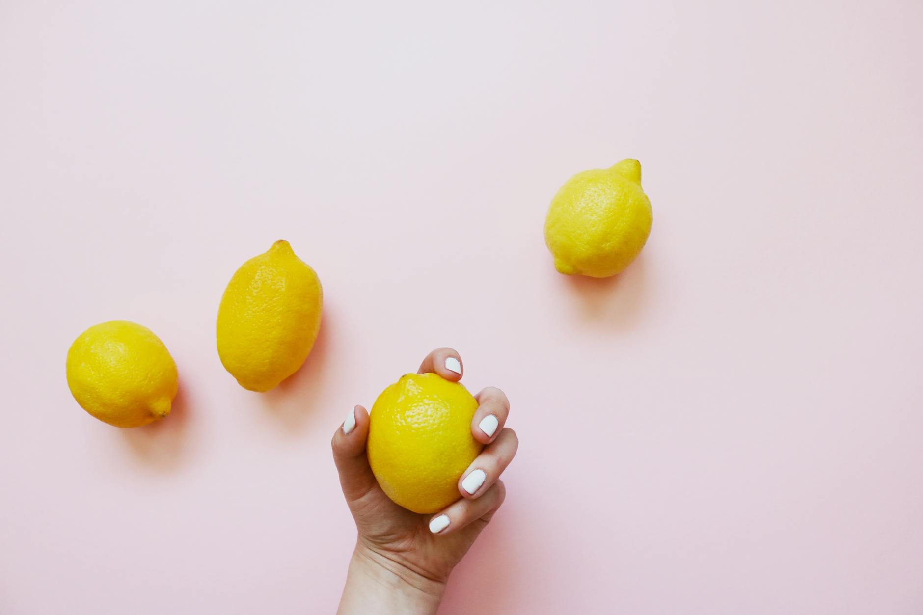 A hand holding a fresh lemon against a soft pink background, evoking gentle, natural pleasure