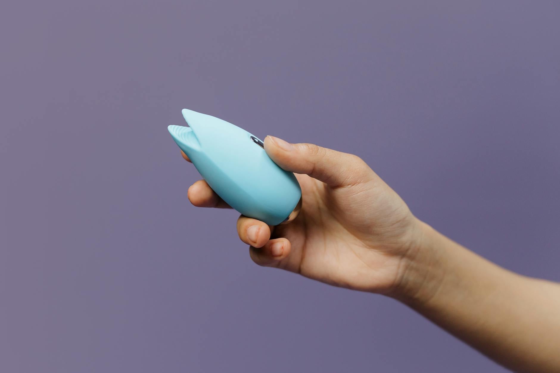 A silicone vibrator held in hand against a purple background, symbolizing self-love and solo pleasure.
