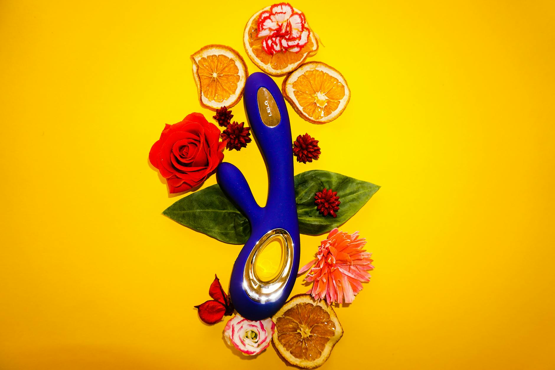 Un vibromasseur bleu entouré de fleurs et d'oranges sur un fond jaune, symbolisant plaisir et sensibilité.